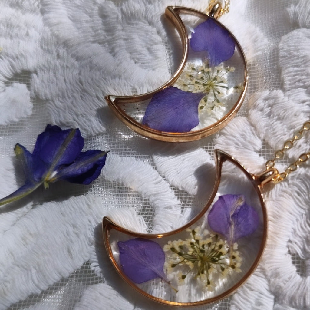 Close-up of crescent resin pendant encasing real dried flowers with silver-plated chain