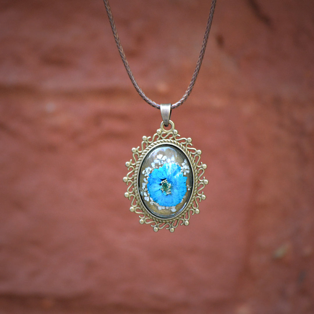 Artistic blue botanical pendant with real flowers encased in transparent resin and silver-toned bezel